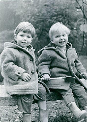 תצלום וינטג 'של תמונה של שני ילד שיושב על ספסל, לובש ז'קט, מחייך.